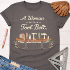 Women's funny woodworking graphic tee shirt for female woodworkers, makers, and DIY builders — Sawdust & Ponytails. Dark gray cotton tee with "A Woman With A Tool Belt" text and a graphic tool belt.