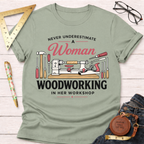 Women's funny woodworking graphic tee shirt for female woodworkers, makers, and DIY builders — Sawdust & Ponytails. Sage green crewneck t-shirt with "Never Underestimate A Woman Woodworking In Her Workshop" text and woodworking tools graphic.