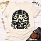 Cream cotton t-shirt with a black graphic of Abraham Lincoln, "America EST. 1776" banner, and American flags.