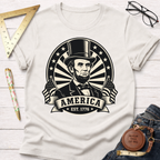 Cream cotton t-shirt with a black Abraham Lincoln portrait, "AMERICA EST. 1776" banner, and US flags.