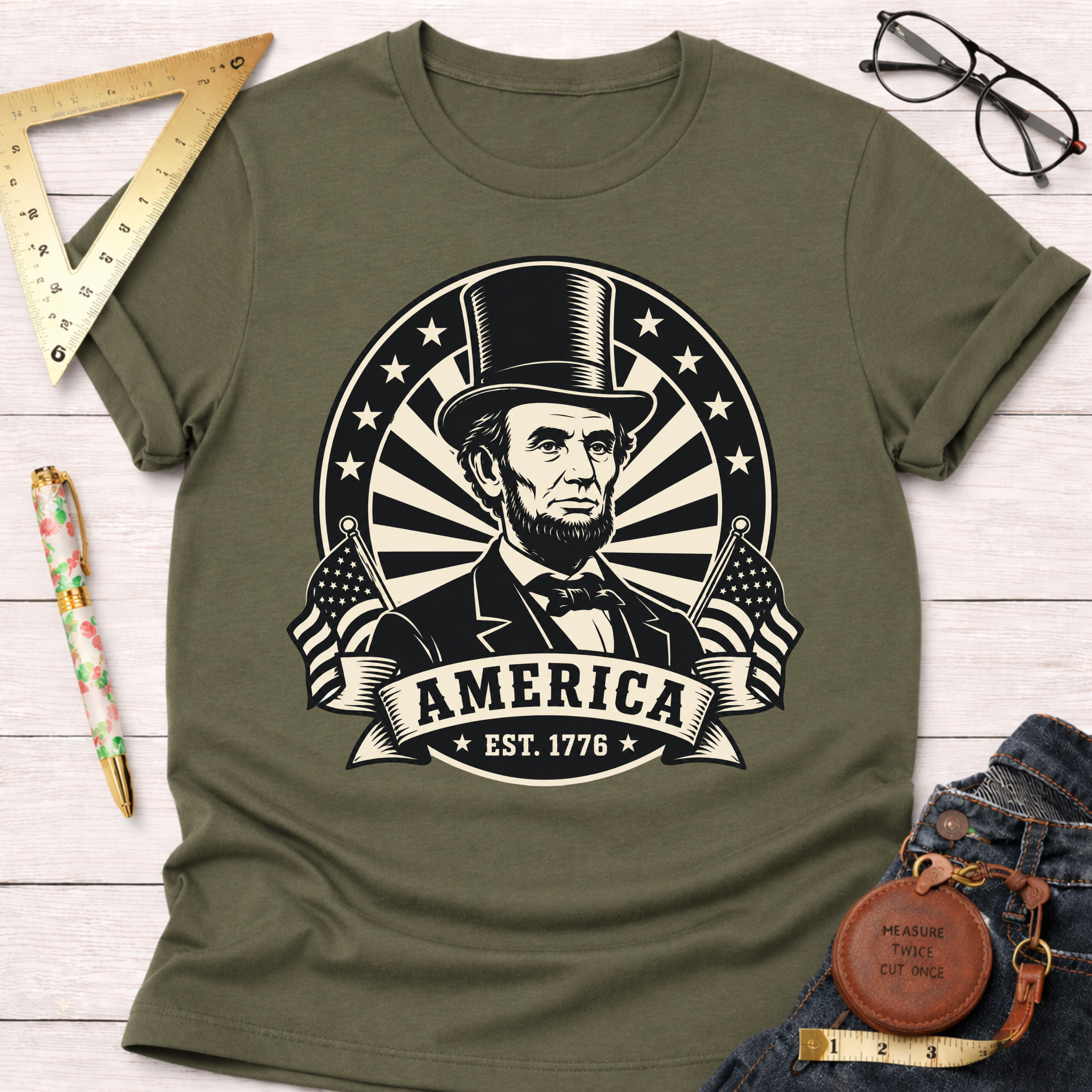 Olive green cotton t-shirt with a black and white Abraham Lincoln graphic, "AMERICA EST. 1776" text, and flags.