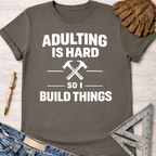 Charcoal gray women's "Adulting Is Hard So I Build Things" graphic tee with crossed hammers, for female woodworkers.