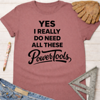 Women's funny woodworking graphic tee shirt for female woodworkers, makers, and DIY builders — Sawdust & Ponytails. Mauve t-shirt with "YES I REALLY DO NEED ALL THESE PowerTools" in black text.