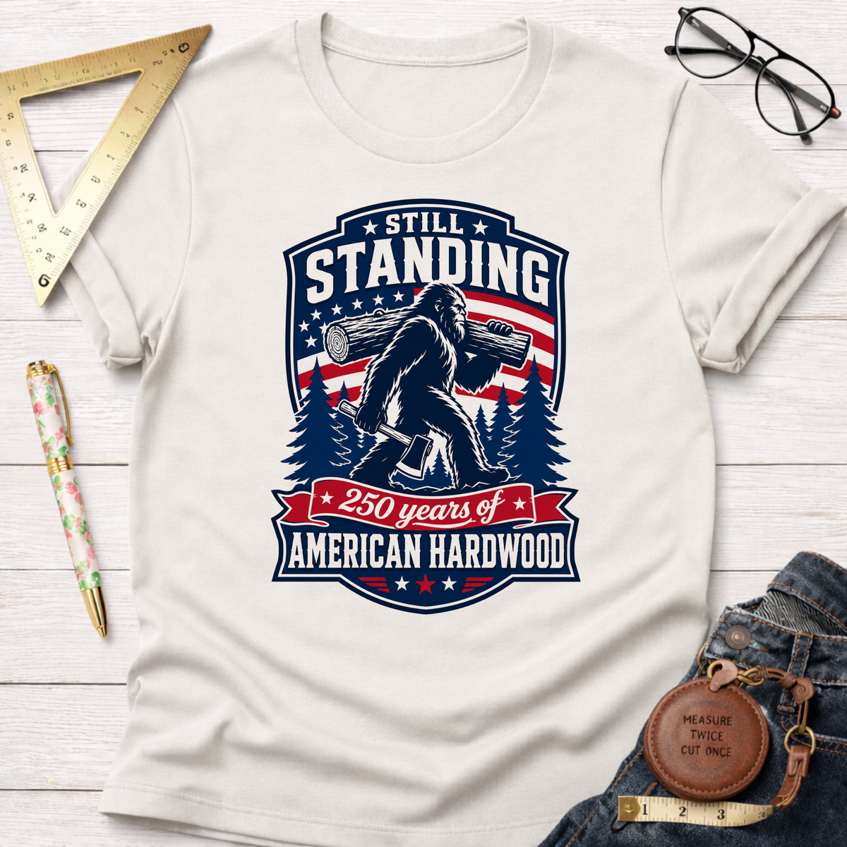 White cotton t-shirt with "Still Standing, 250 years of American Hardwood" graphic featuring Bigfoot carrying a log.