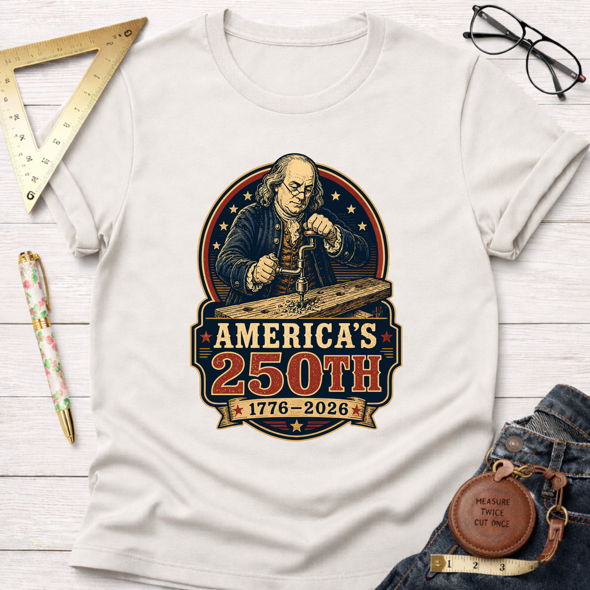 White cotton t-shirt with a graphic of Benjamin Franklin woodworking, "America's 250th 1776-2026" design.