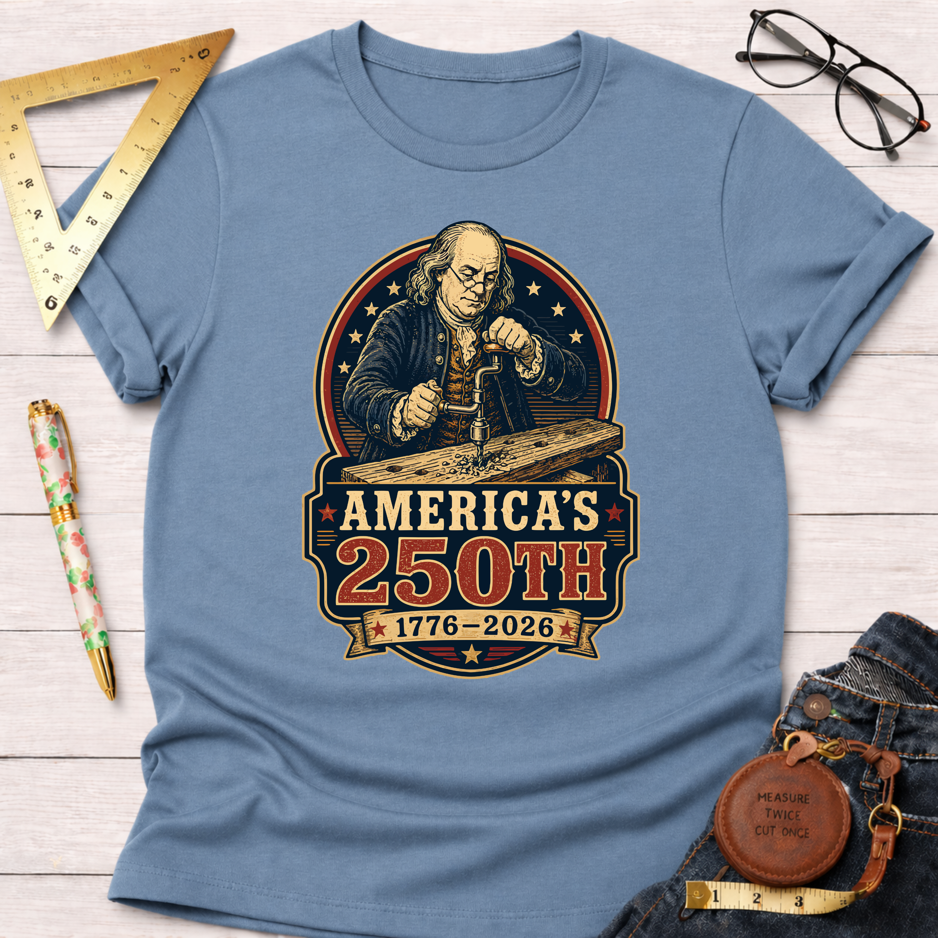 Light blue cotton t-shirt with a graphic of Benjamin Franklin drilling wood, "America's 250th 1776-2026.