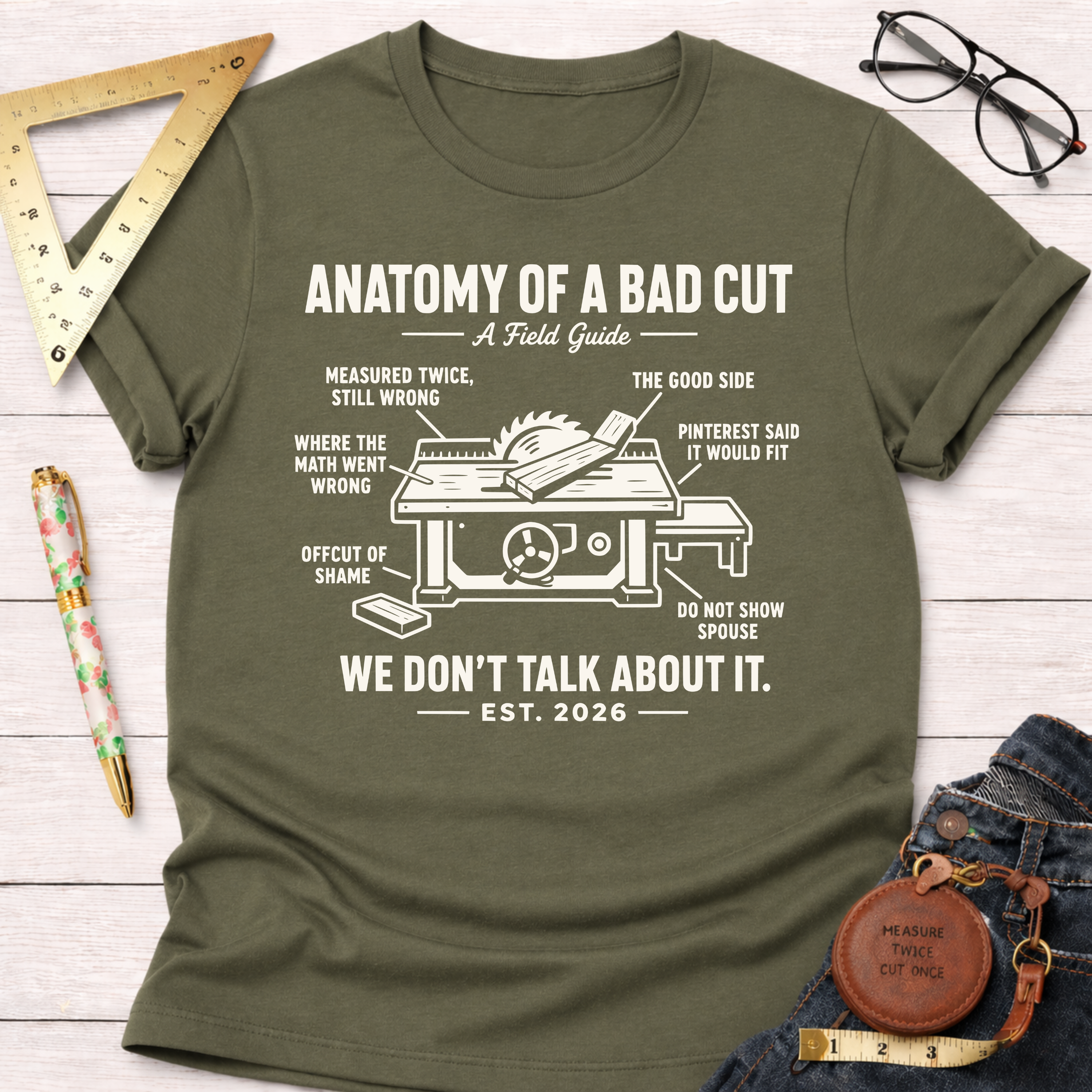 Women's funny woodworking graphic tee shirt for female woodworkers, makers, and DIY builders — Sawdust & Ponytails. Olive green cotton tee with "Anatomy of a Bad Cut" graphic.