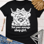 Black cotton tee with a white graphic of a Highland cow in goggles and bow, "Not your average shop girl." Women's funny woodworking graphic tee shirt for female woodworkers, makers, and DIY builders — Sawdust & Ponytails.