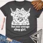 Women's funny woodworking graphic tee shirt for female woodworkers, makers, and DIY builders — Sawdust & Ponytails. Dark gray crewneck t-shirt with a white graphic of a Highland cow wearing a bow and goggles, above "Not your average shop girl.