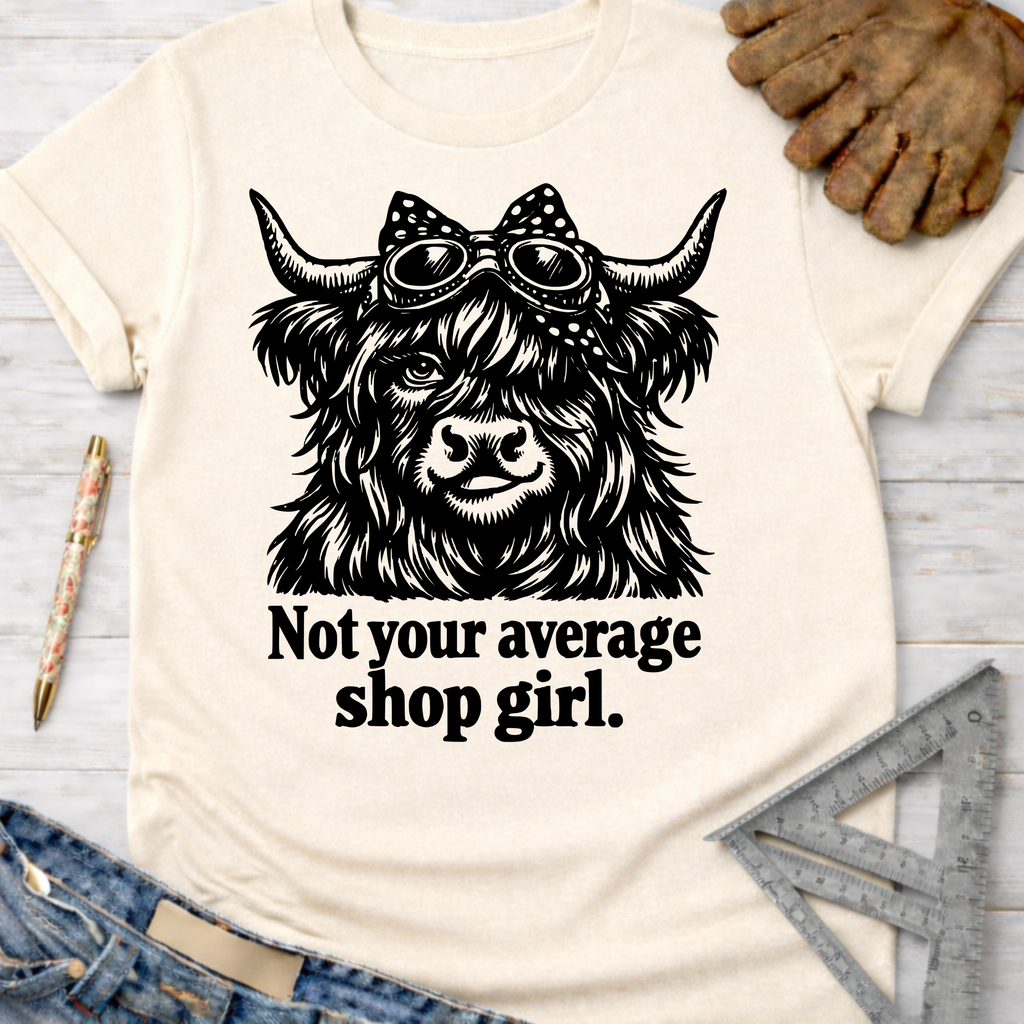 Women's funny woodworking graphic tee shirt for female woodworkers, makers, and DIY builders — Sawdust & Ponytails. Cream t-shirt with a black graphic of a Highland cow wearing goggles and a polka dot bow, with the text "Not your average shop girl.