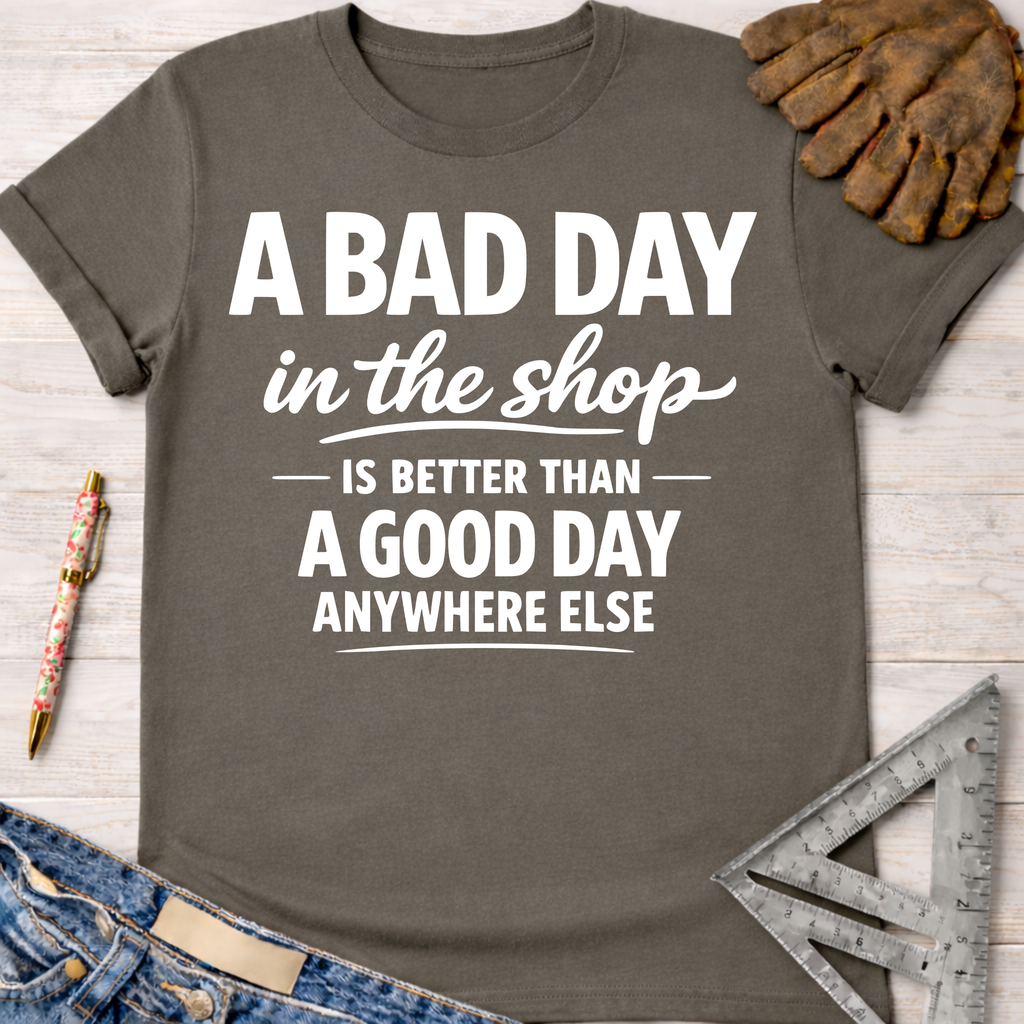 Charcoal gray women's funny woodworking graphic tee with "A BAD DAY in the shop IS BETTER THAN A GOOD DAY ANYWHERE ELSE" text. Sawdust & Ponytails.