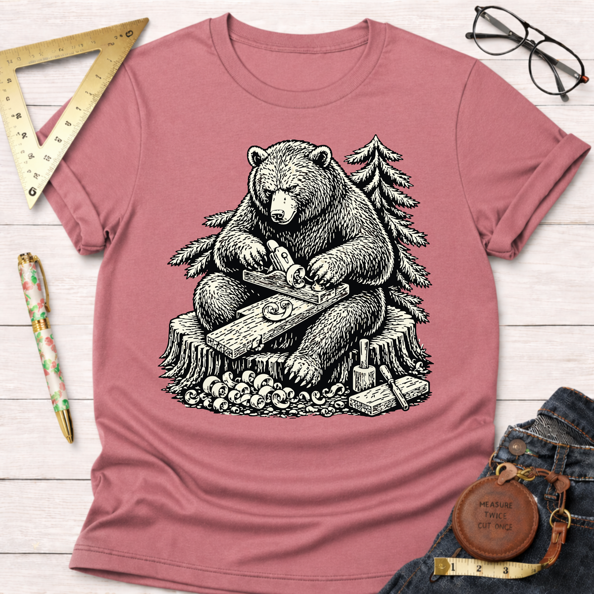 Women's funny woodworking graphic tee shirt for female woodworkers, makers, and DIY builders — Sawdust & Ponytails. Dusty rose cotton t-shirt with a black and white graphic of a bear hand planing wood.
