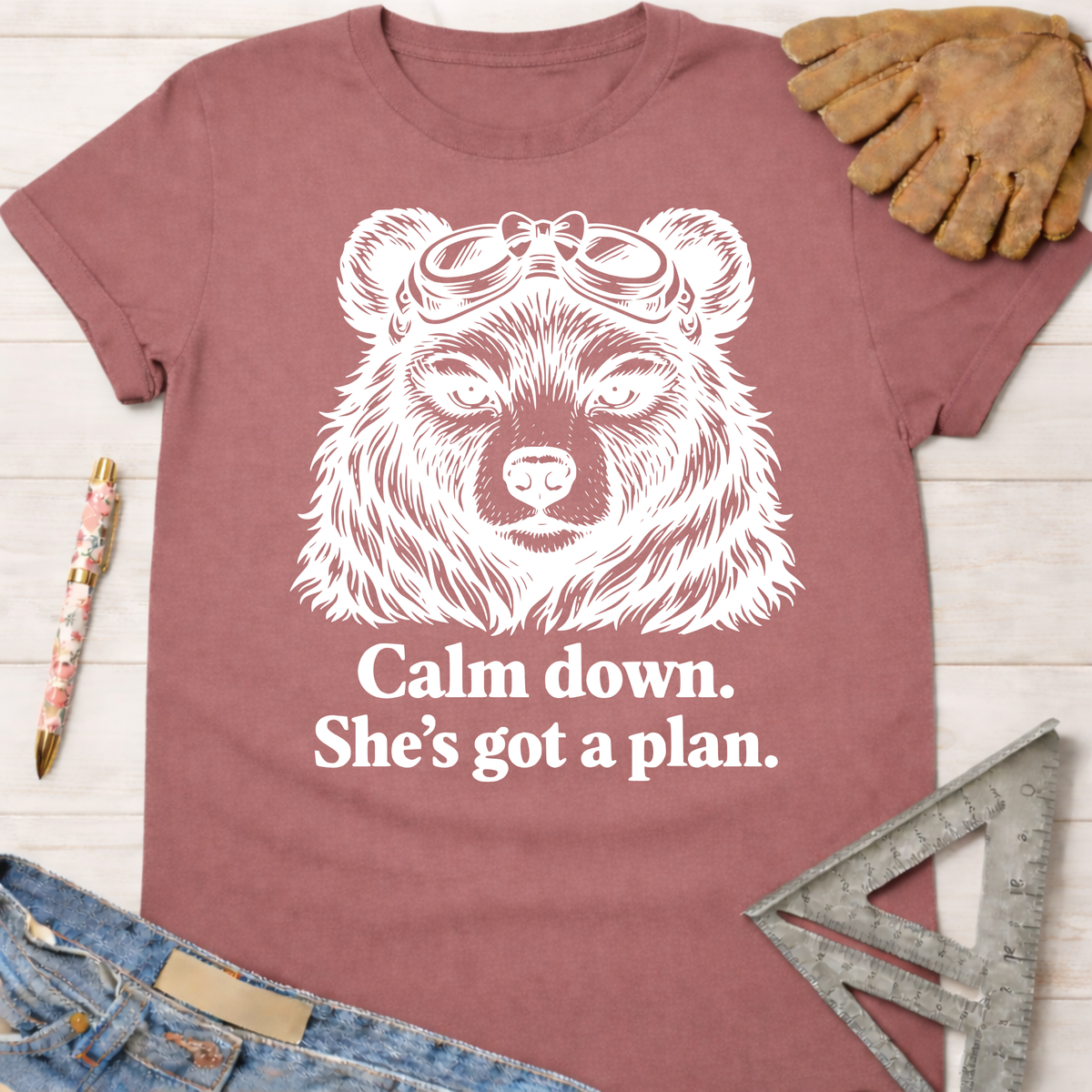 Women's funny woodworking graphic tee shirt for female woodworkers, makers, and DIY builders — Sawdust & Ponytails. Mauve t-shirt with a white graphic of a bear wearing goggles and the text "Calm down. She's got a plan.