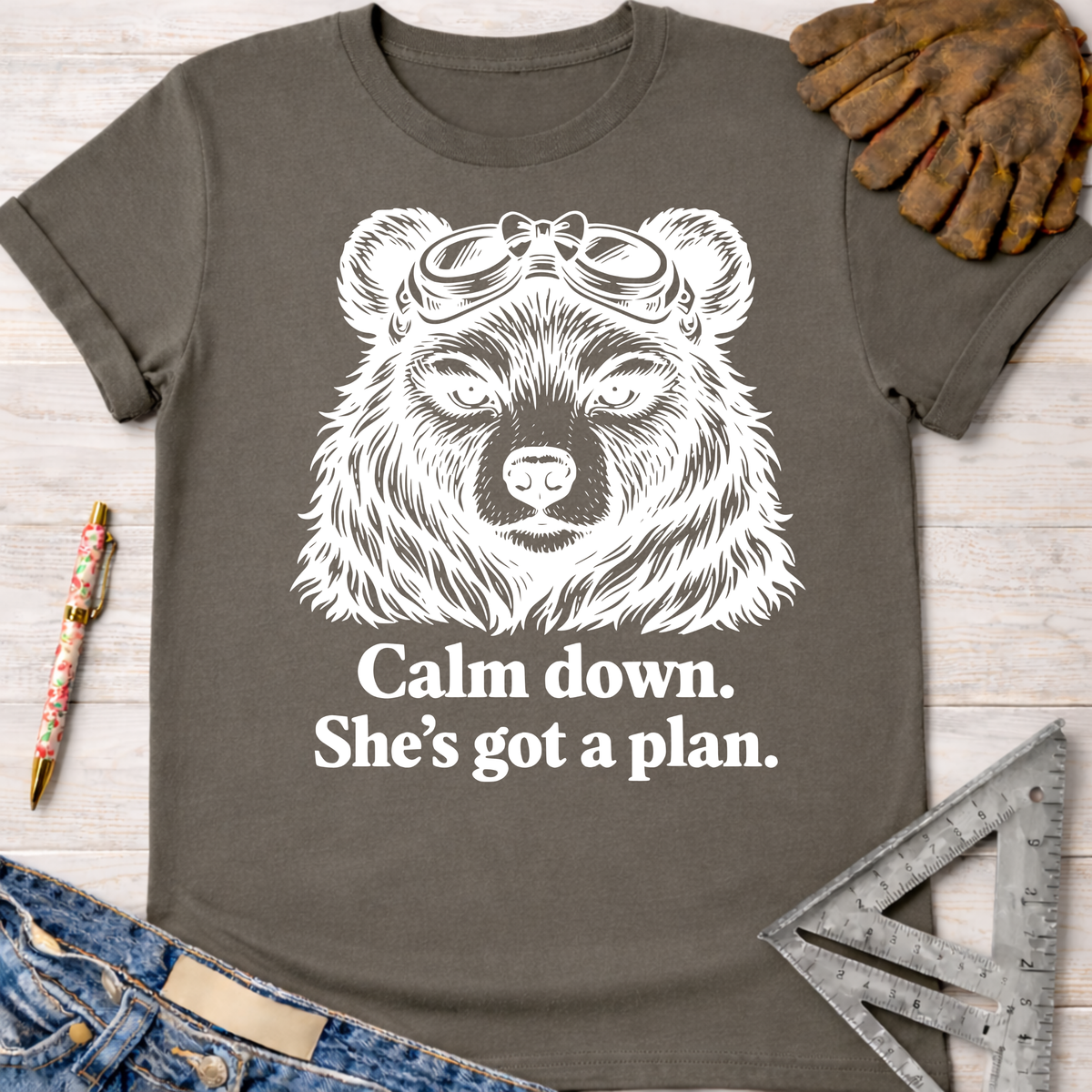 Women's funny woodworking graphic tee shirt for female woodworkers, makers, and DIY builders — Sawdust & Ponytails. Charcoal tee with white bear in goggles, "Calm down. She's got a plan." text.