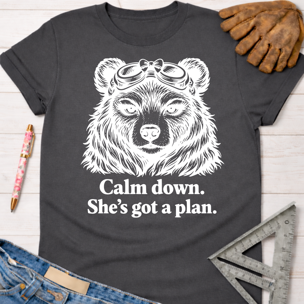 Women's funny woodworking graphic tee shirt for female woodworkers, makers, and DIY builders — Sawdust & Ponytails. Dark gray tee with a white bear wearing goggles and "Calm down. She's got a plan." text.