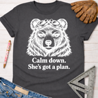 Women's funny woodworking graphic tee shirt for female woodworkers, makers, and DIY builders — Sawdust & Ponytails. Dark gray tee with a white bear wearing goggles and "Calm down. She's got a plan." text.