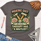 Women's funny woodworking graphic tee shirt for female woodworkers, makers, and DIY builders — Sawdust & Ponytails. Dark gray cotton tee with "Making Shit Because Therapy Has A Waitlist" graphic featuring hammers and pink flowers.