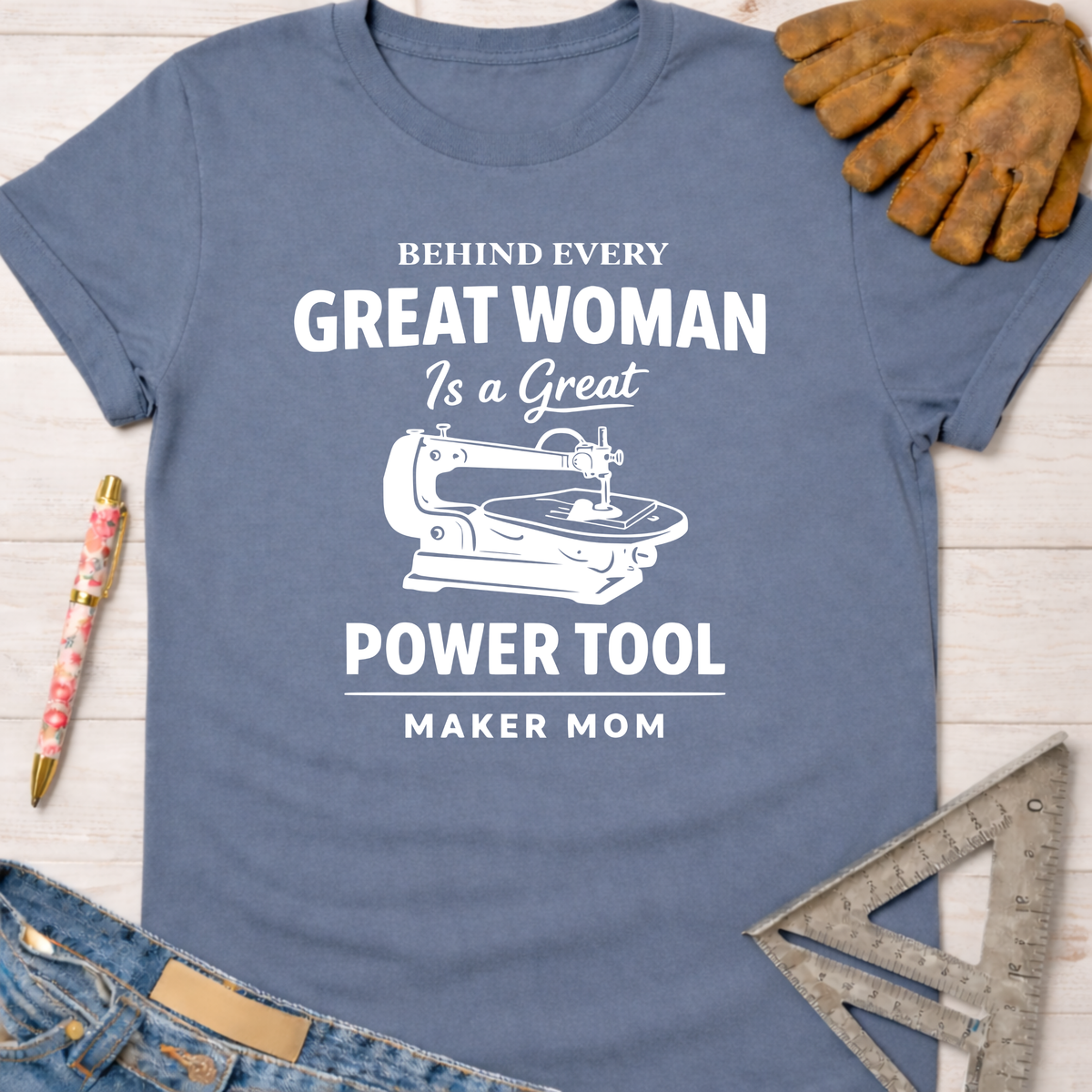 Women's funny woodworking graphic tee shirt for female woodworkers, makers, and DIY builders — Sawdust & Ponytails. Blue cotton tee with "Behind Every Great Woman Is a Great Power Tool Maker Mom" text and sewing machine graphic.