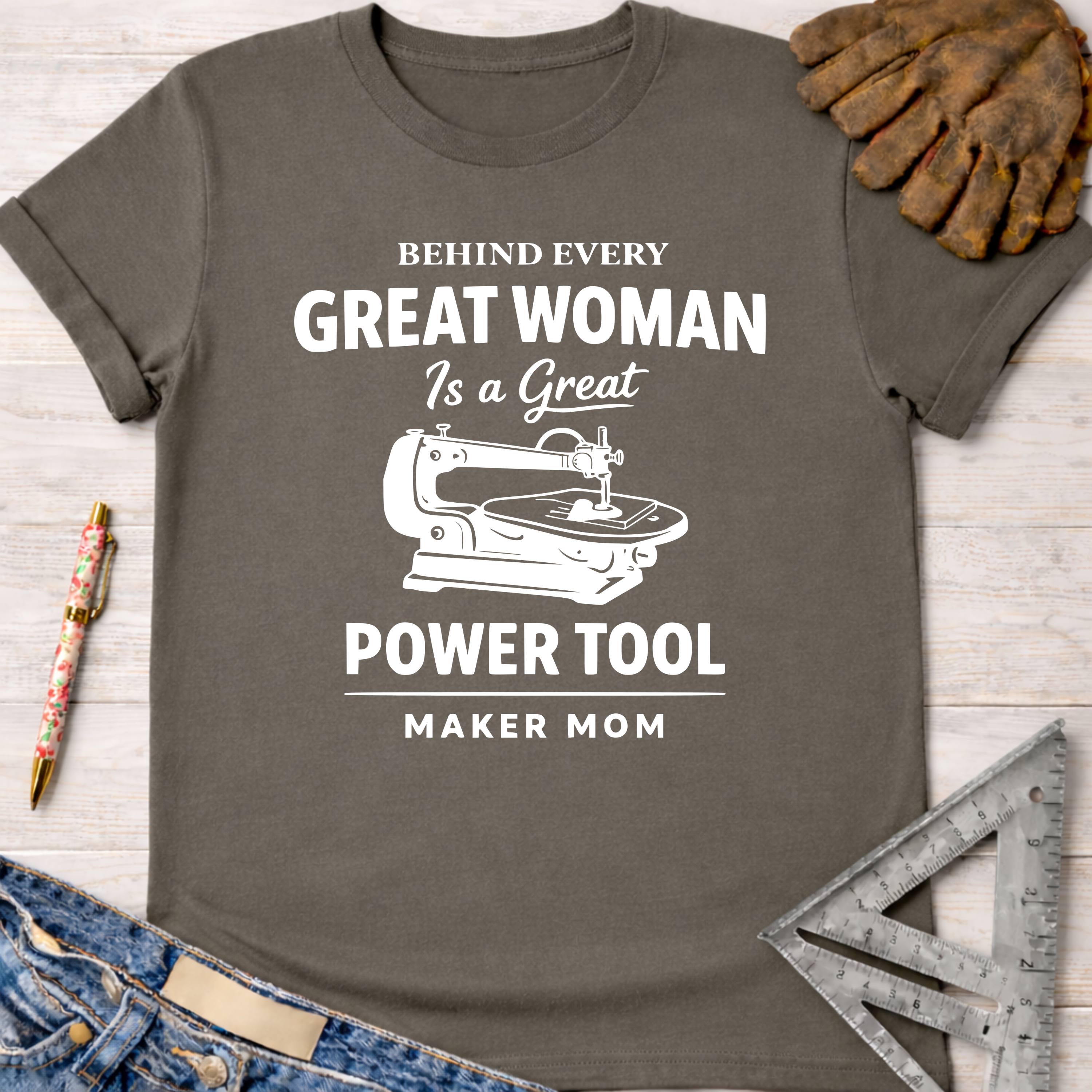 Women's funny woodworking graphic tee shirt for female woodworkers, makers, and DIY builders — Sawdust & Ponytails. Dark gray t-shirt with "Behind Every Great Woman Is a Great Power Tool Maker Mom" text and scroll saw graphic.