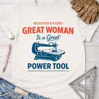 Women's funny woodworking graphic tee shirt for female woodworkers, makers, and DIY builders — Sawdust & Ponytails. White cotton tee with "Behind Every Great Woman Is a Great Power Tool" text and scroll saw graphic.