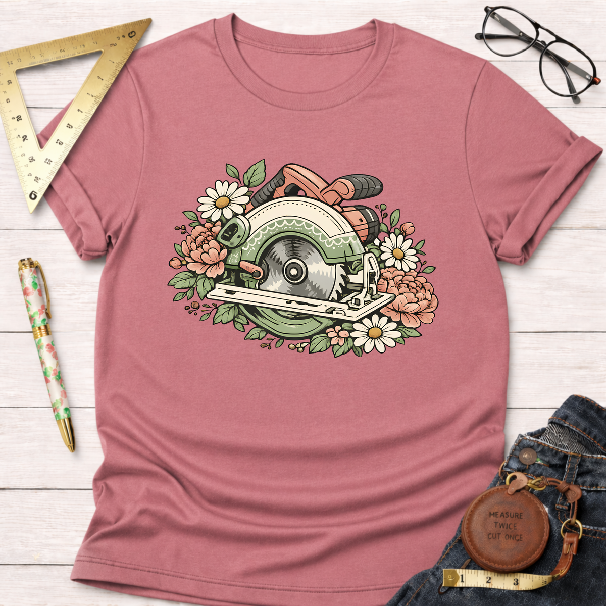 Dusty rose t-shirt with a floral circular saw graphic, styled with jeans, glasses, and a ruler.