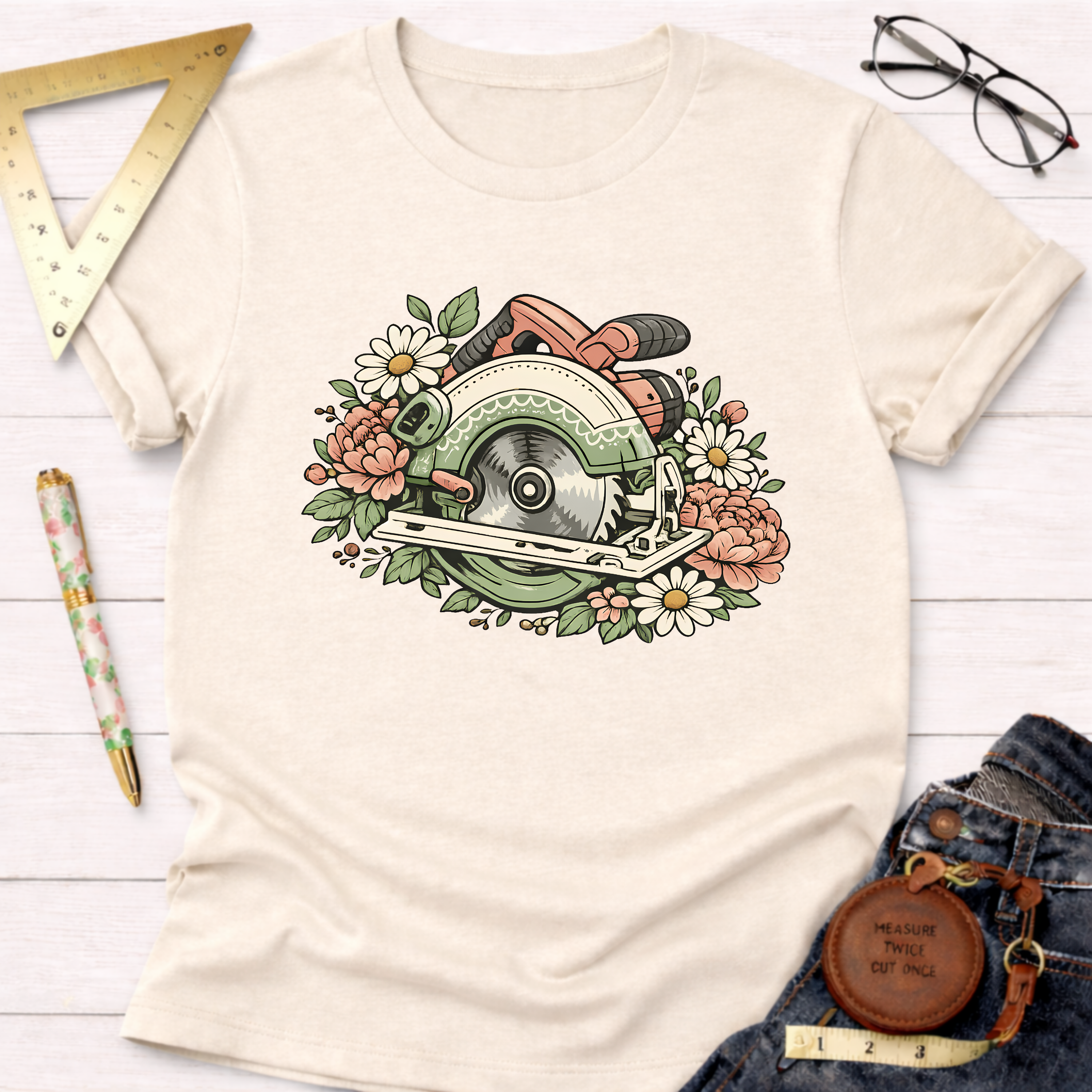 Cream t-shirt with a colorful graphic of a circular saw surrounded by pink and white flowers.