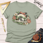 Sage green Bloom & Blade T-shirt with a floral circular saw design, folded on a white wooden surface.