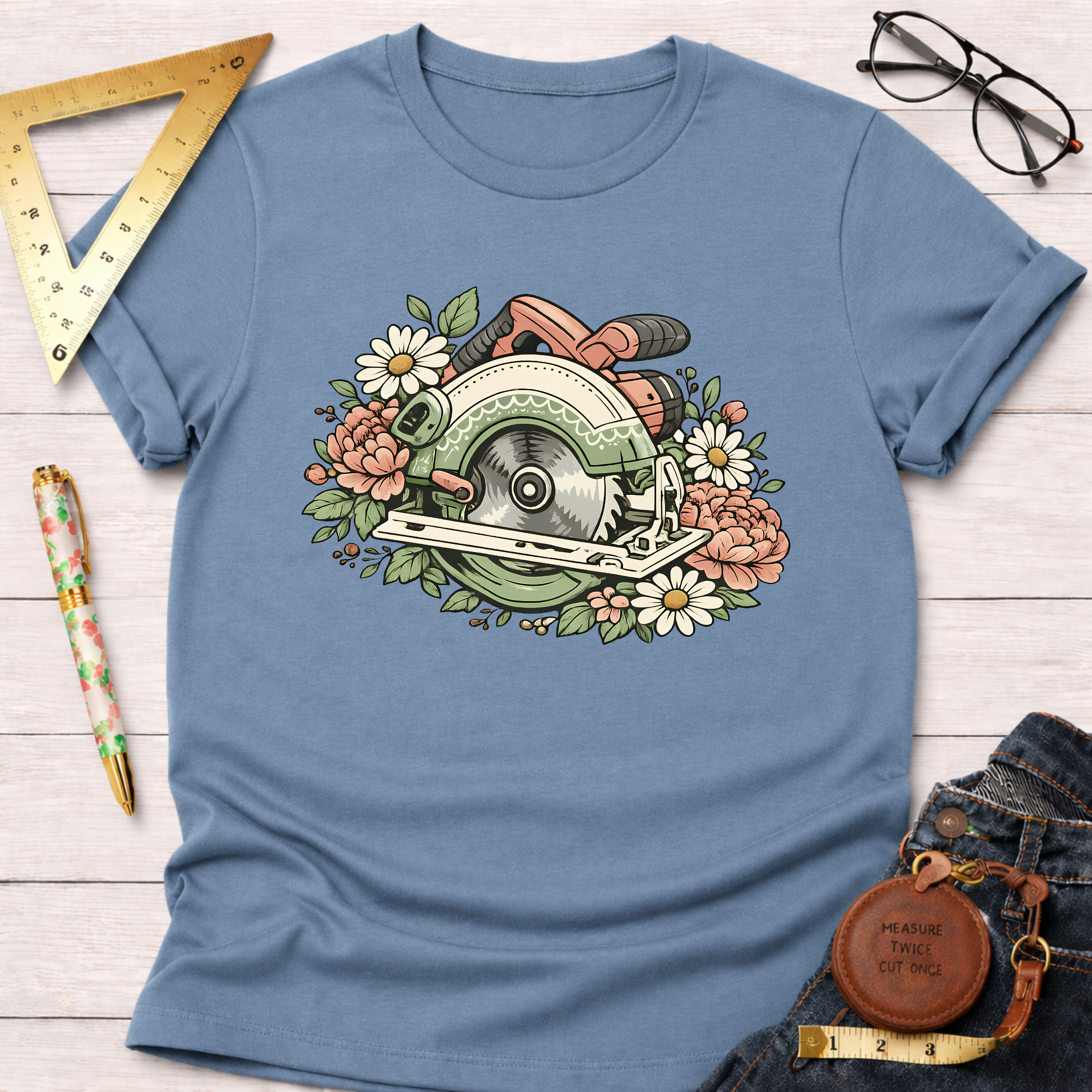 Blue Bloom & Blade T-shirt with a circular saw and floral design, surrounded by tools and jeans.