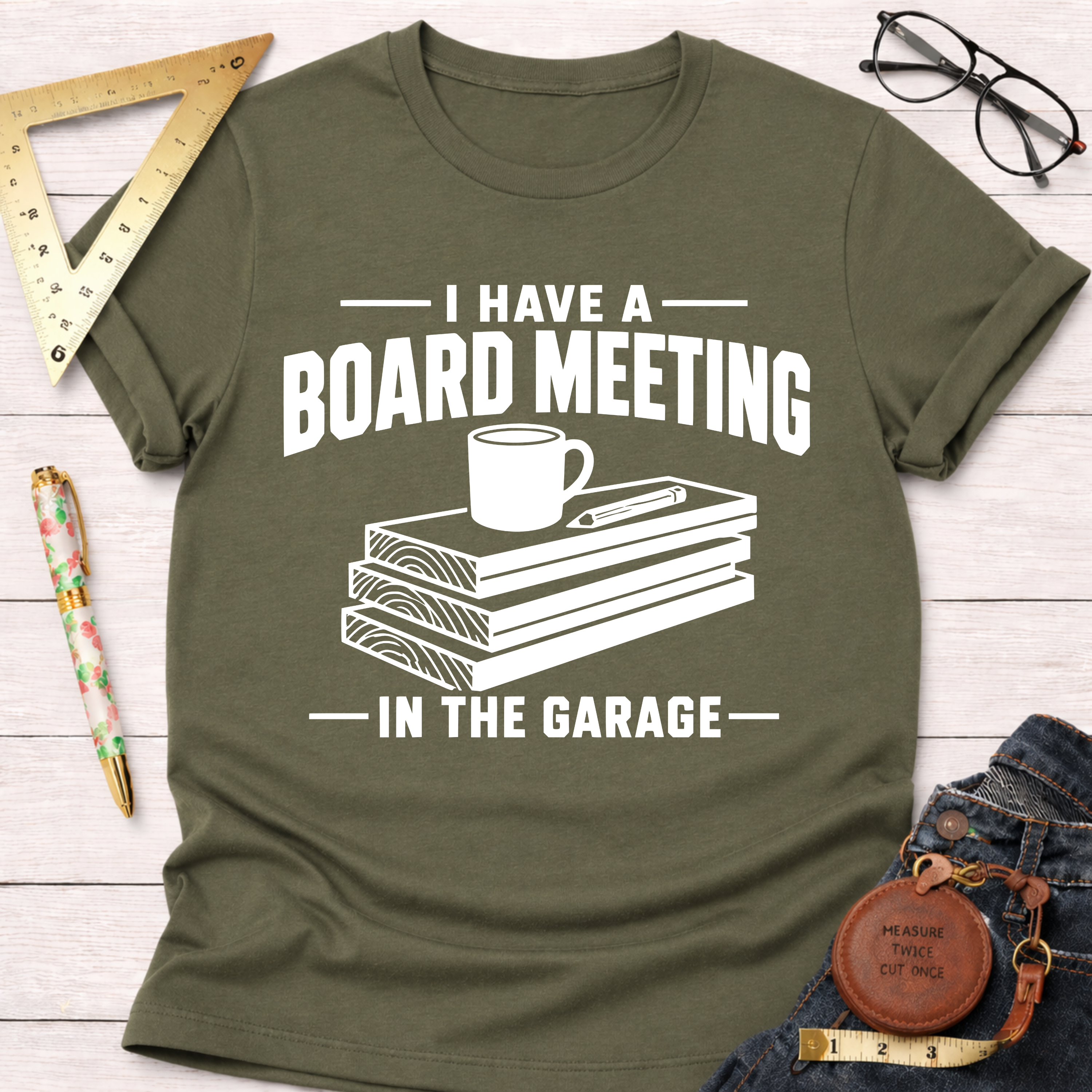 Olive green "Board Meeting In The Garage" t-shirt with stacked wood, coffee cup, and pencil graphic.
