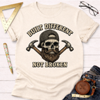 Cream t-shirt with a bearded skull wearing a cap, crossed hammers, and "Built Different Not Broken" text.