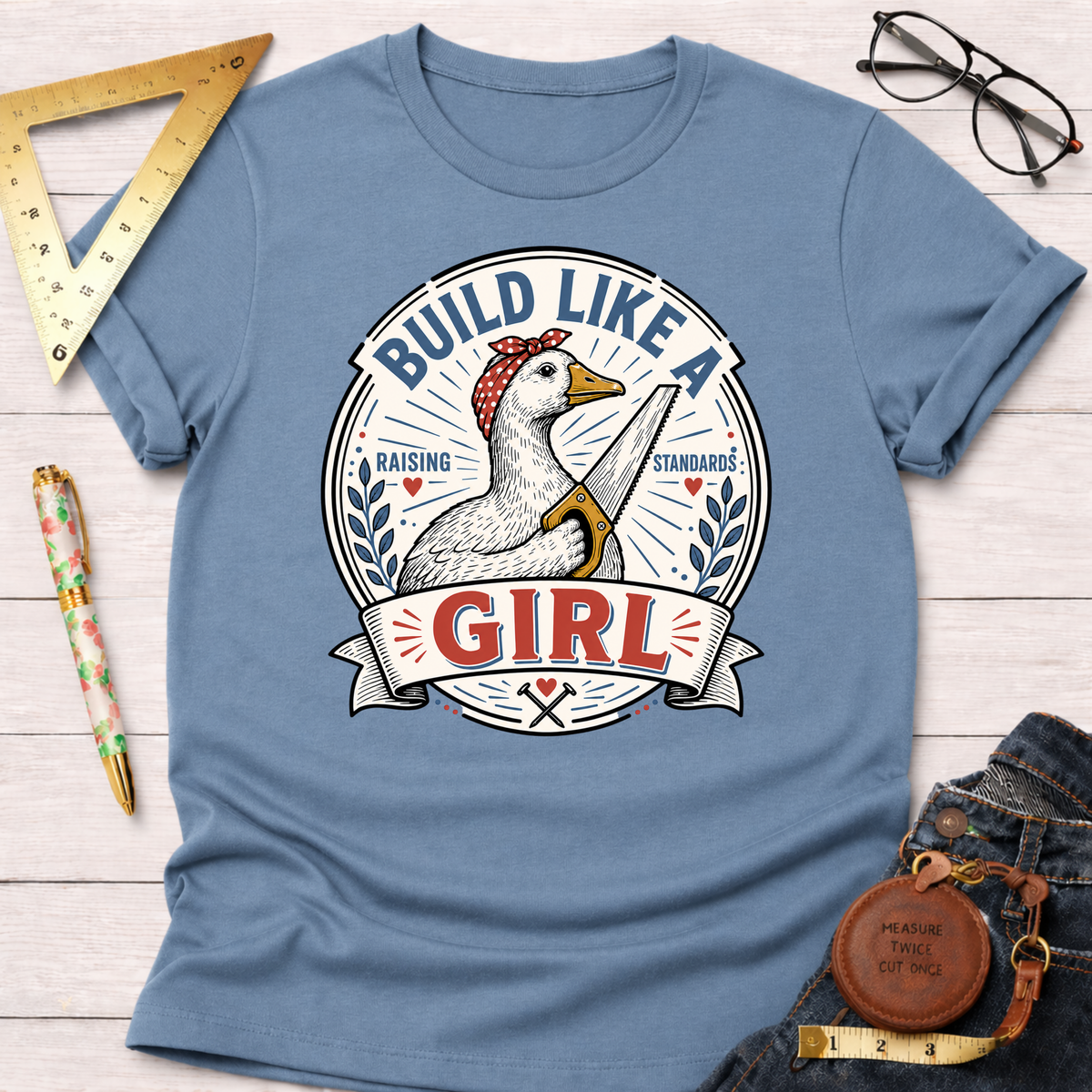 Light blue cotton t-shirt with a "Build Like A Girl" graphic featuring a goose holding a saw.