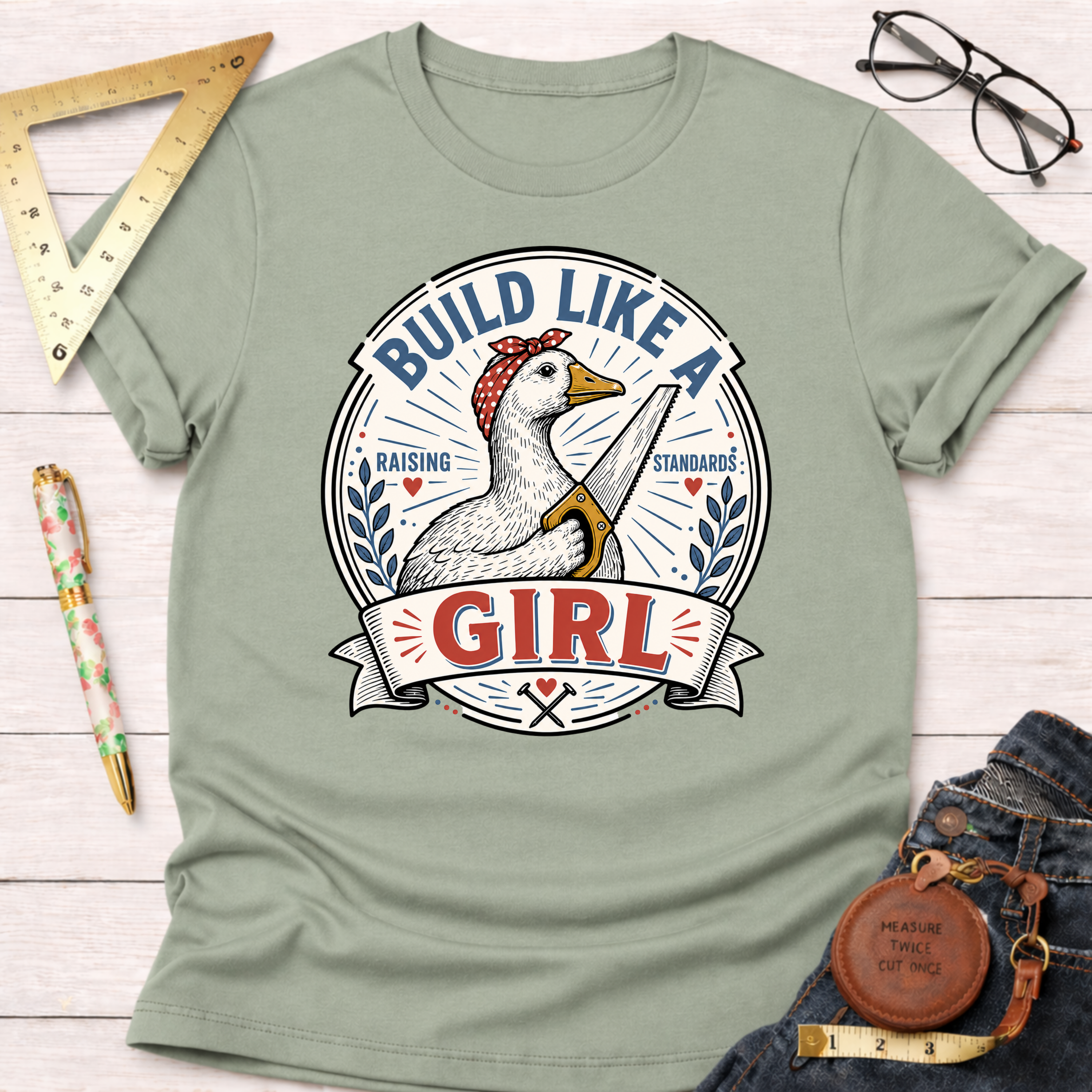 Sage green cotton t-shirt with a "Build Like A Girl" graphic featuring a goose holding a saw.