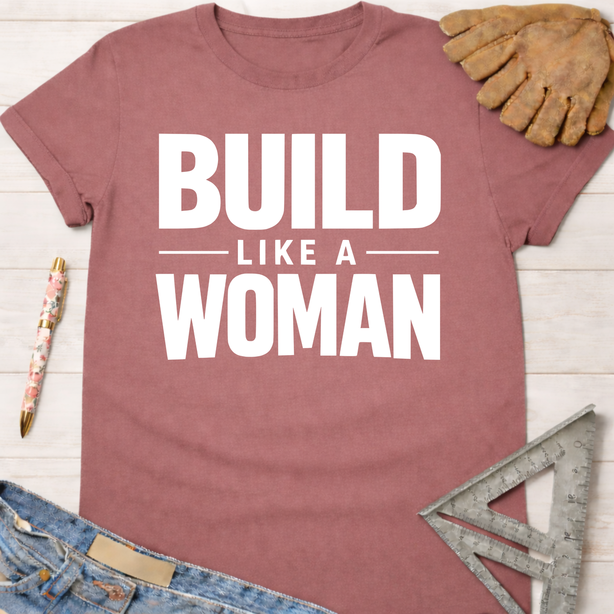 Women's funny woodworking graphic tee shirt for female woodworkers, makers, and DIY builders — Sawdust & Ponytails. Mauve cotton tee with "BUILD LIKE A WOMAN" in white text.