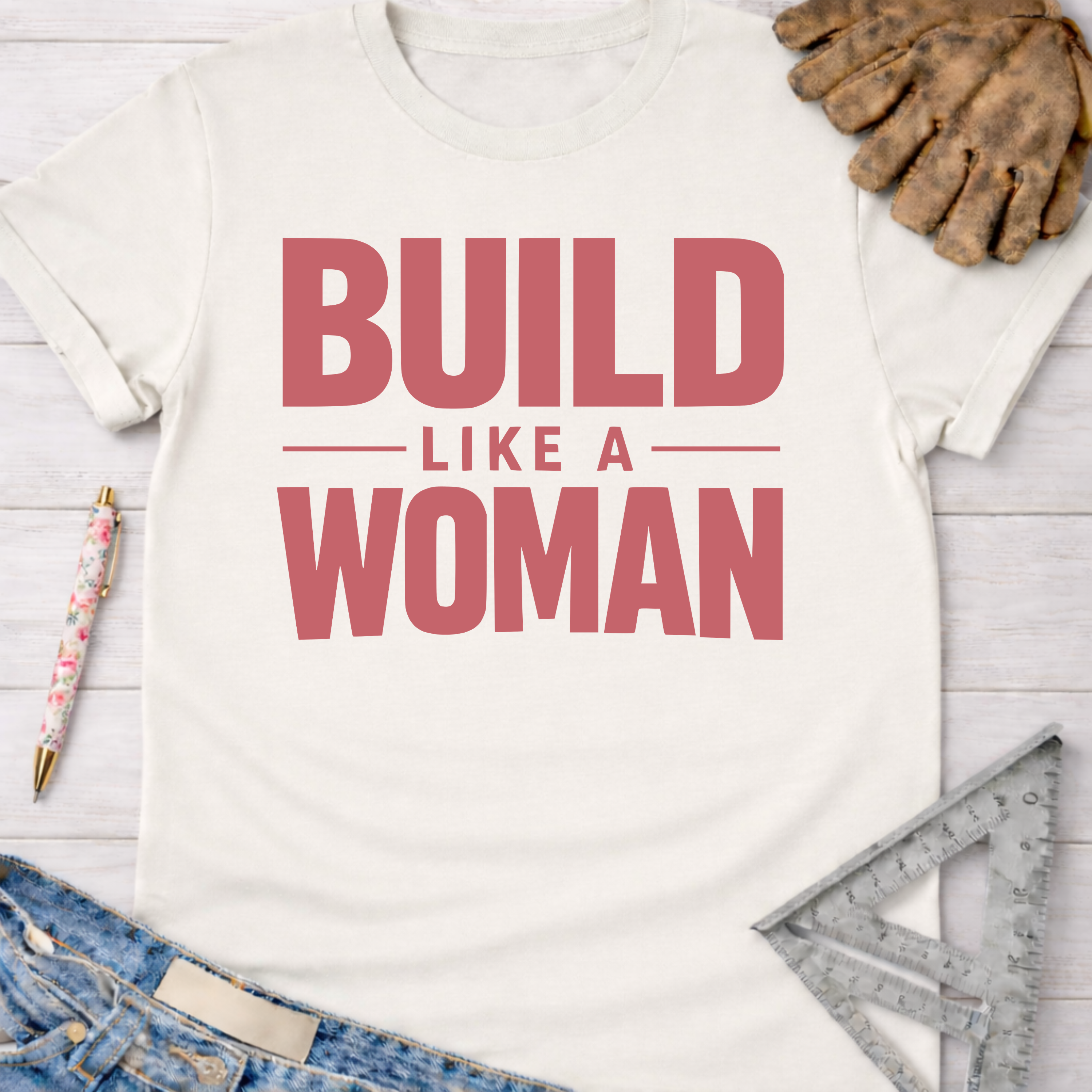 Women's funny woodworking graphic tee shirt for female woodworkers, makers, and DIY builders — Sawdust & Ponytails. Cream cotton tee with "BUILD LIKE A WOMAN" in red text.