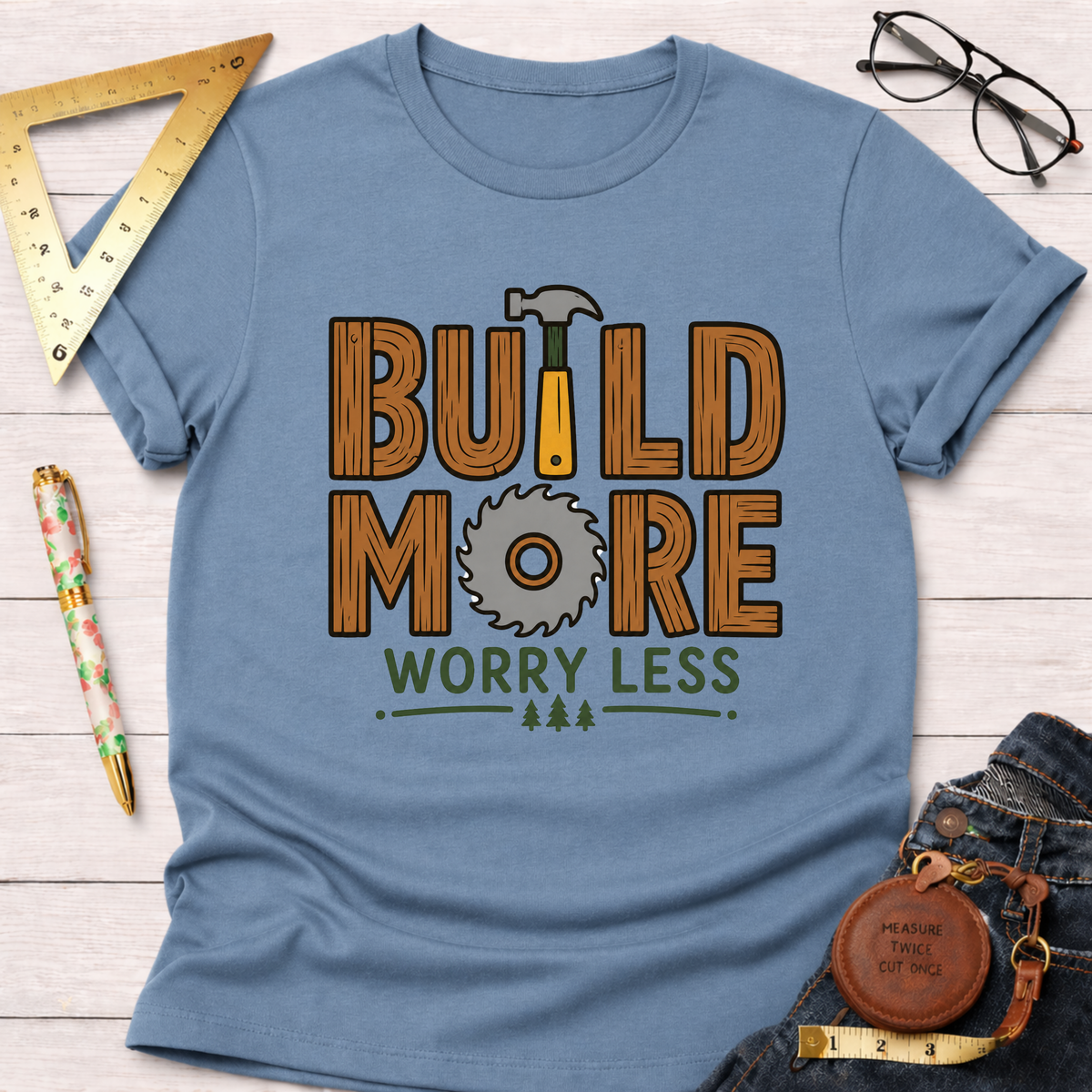 Women's funny woodworking graphic tee shirt for female woodworkers, makers, and DIY builders — Sawdust & Ponytails. Light blue tee with "BUILD MORE WORRY LESS" graphic.