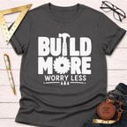 Women's funny woodworking graphic tee shirt for female woodworkers, makers, and DIY builders — Sawdust & Ponytails. Dark gray tee with "BUILD MORE WORRY LESS" text, hammer, and saw blade graphic.