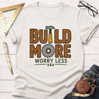 Women's funny woodworking graphic tee shirt for female woodworkers, makers, and DIY builders — Sawdust & Ponytails. Cream t-shirt with "BUILD MORE WORRY LESS" wood-textured graphic.