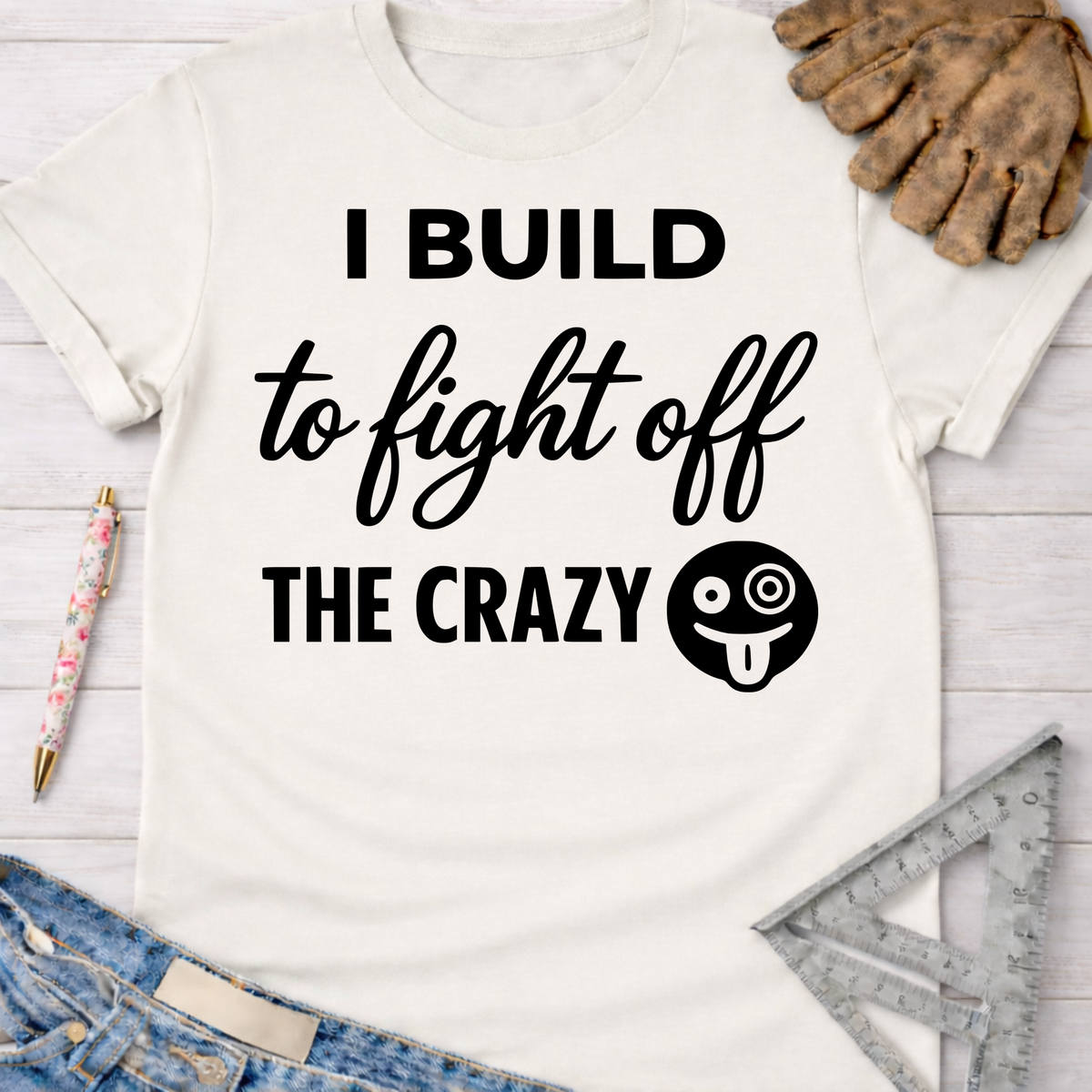 Women's funny woodworking graphic tee shirt for female woodworkers, makers, and DIY builders — Sawdust & Ponytails. White cotton tee with "I BUILD to fight off THE CRAZY" text and a silly face emoji.