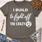 Women's funny woodworking graphic tee shirt for female woodworkers, makers, and DIY builders — Sawdust & Ponytails. Dark gray cotton t-shirt with "I BUILD to fight off THE CRAZY" in white text and a silly face emoji.