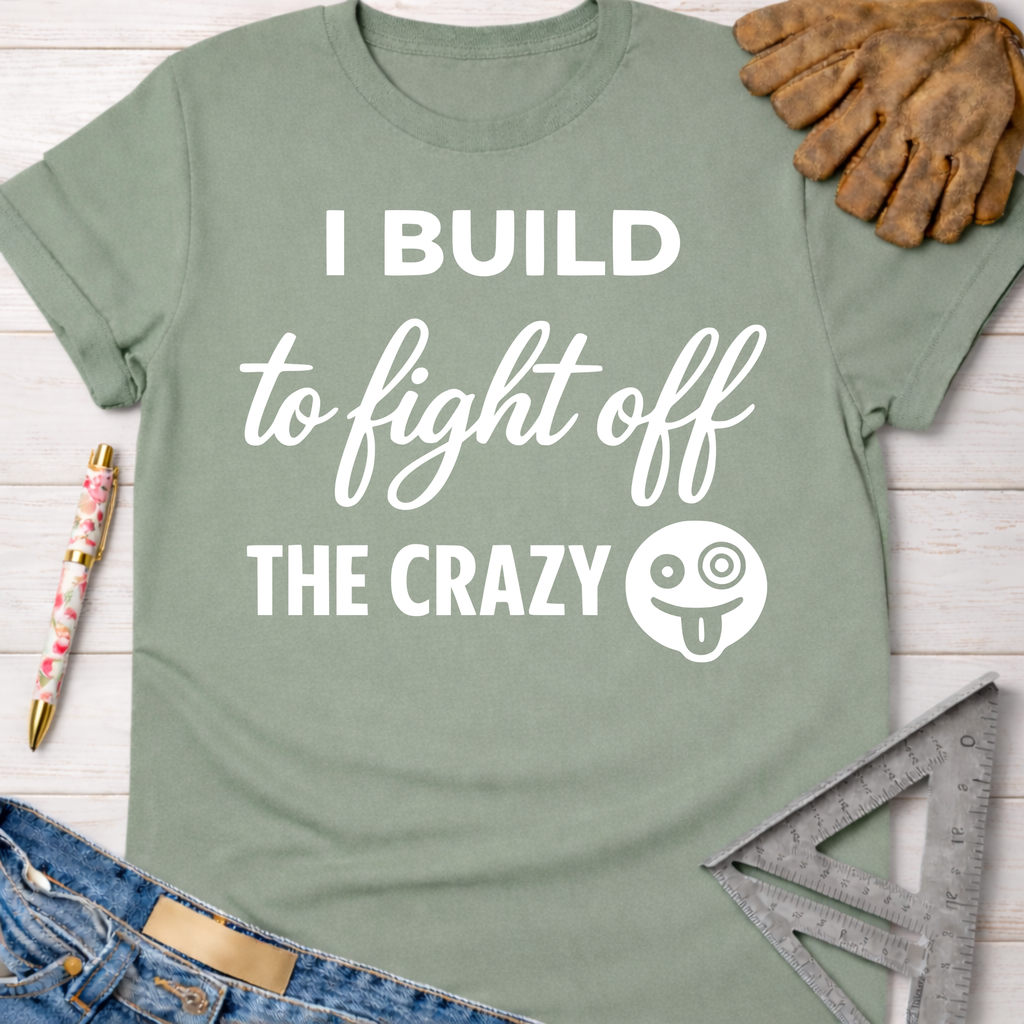 Women's funny woodworking graphic tee shirt for female woodworkers, makers, and DIY builders — Sawdust & Ponytails. Sage green cotton t-shirt with "I BUILD to fight off THE CRAZY" text and emoji.