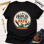 Black t-shirt with "Build Your Own Path" design featuring mountains, trees, saw, plane, and a winding road.