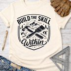 Women's funny woodworking graphic tee shirt for female woodworkers, makers, and DIY builders — Sawdust & Ponytails. Cream t-shirt with "Build The Skill Within" text, hammer, paintbrush, and mountain graphic.