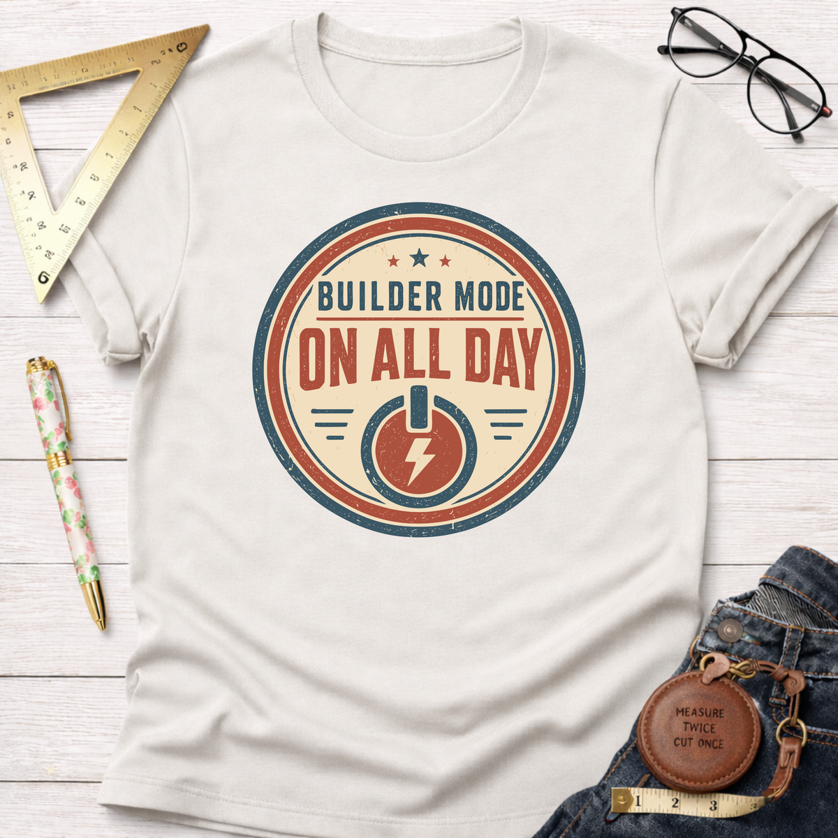 Off-white cotton t-shirt with a "Builder Mode On All Day" graphic, styled with jeans and tools.