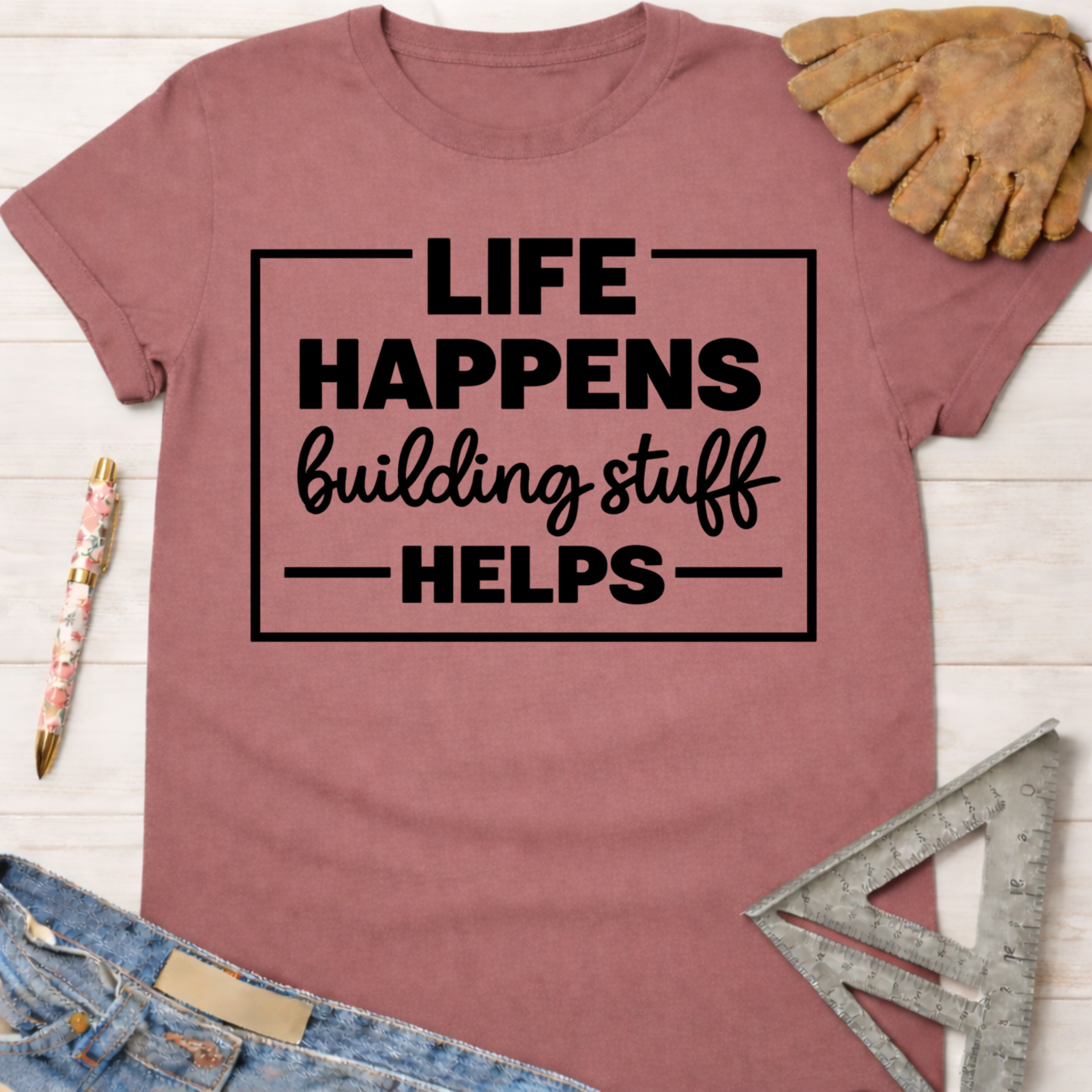 Women's funny woodworking graphic tee shirt for female woodworkers, makers, and DIY builders — Sawdust & Ponytails. Mauve short-sleeve tee with "Life Happens Building Stuff Helps" text.