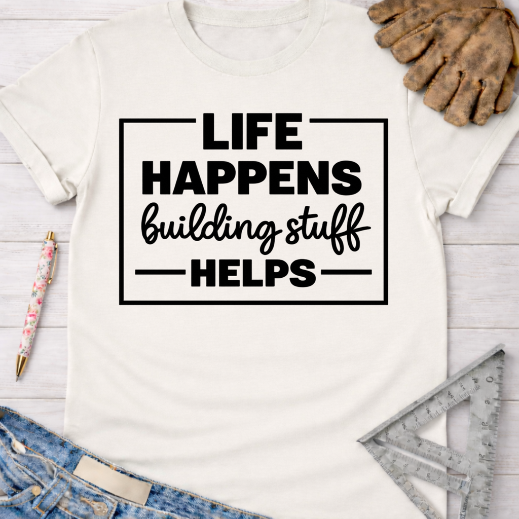 Women's funny woodworking graphic tee shirt for female woodworkers, makers, and DIY builders — Sawdust & Ponytails. Cream cotton tee with "Life Happens Building Stuff Helps" in black text.