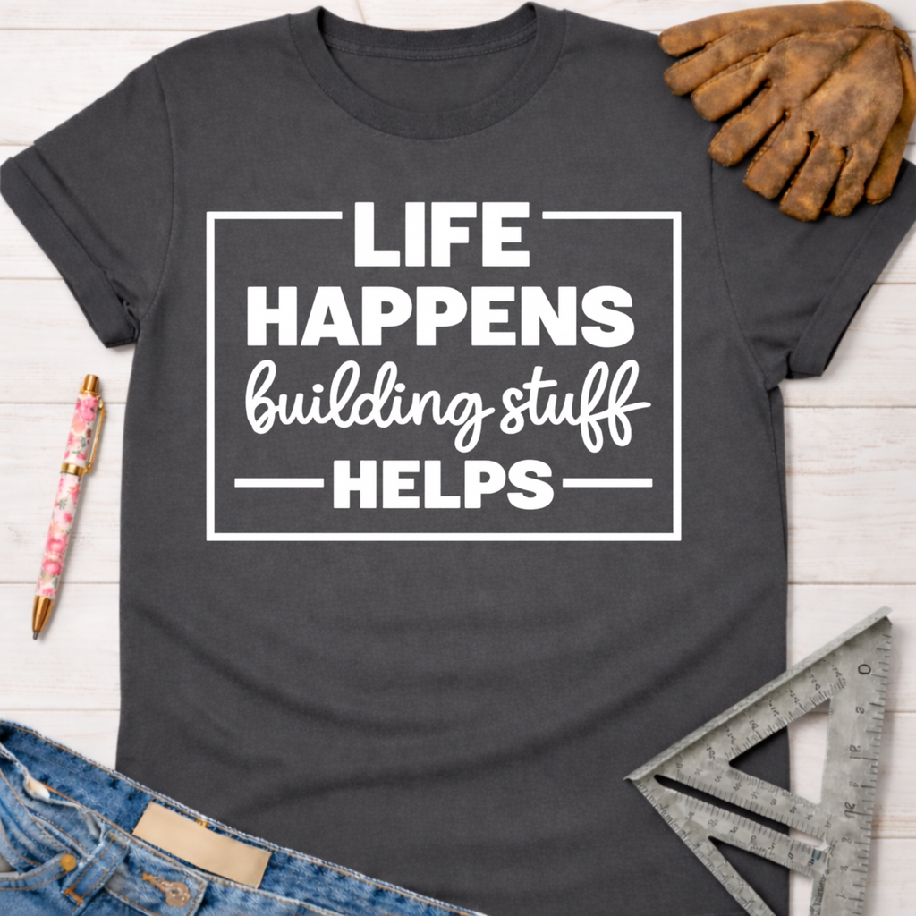 Women's funny woodworking graphic tee shirt for female woodworkers, makers, and DIY builders — Sawdust & Ponytails. Dark gray crewneck t-shirt with "Life Happens Building Stuff Helps" in white text.