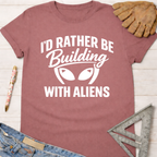 Women's funny woodworking graphic tee shirt for female woodworkers, makers, and DIY builders — Sawdust & Ponytails. Mauve t-shirt with "I'd Rather Be Building With Aliens" graphic.