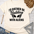 Women's funny woodworking graphic tee shirt for female woodworkers, makers, and DIY builders — Sawdust & Ponytails. Cream t-shirt with "I'd Rather Be Building With Aliens" graphic.