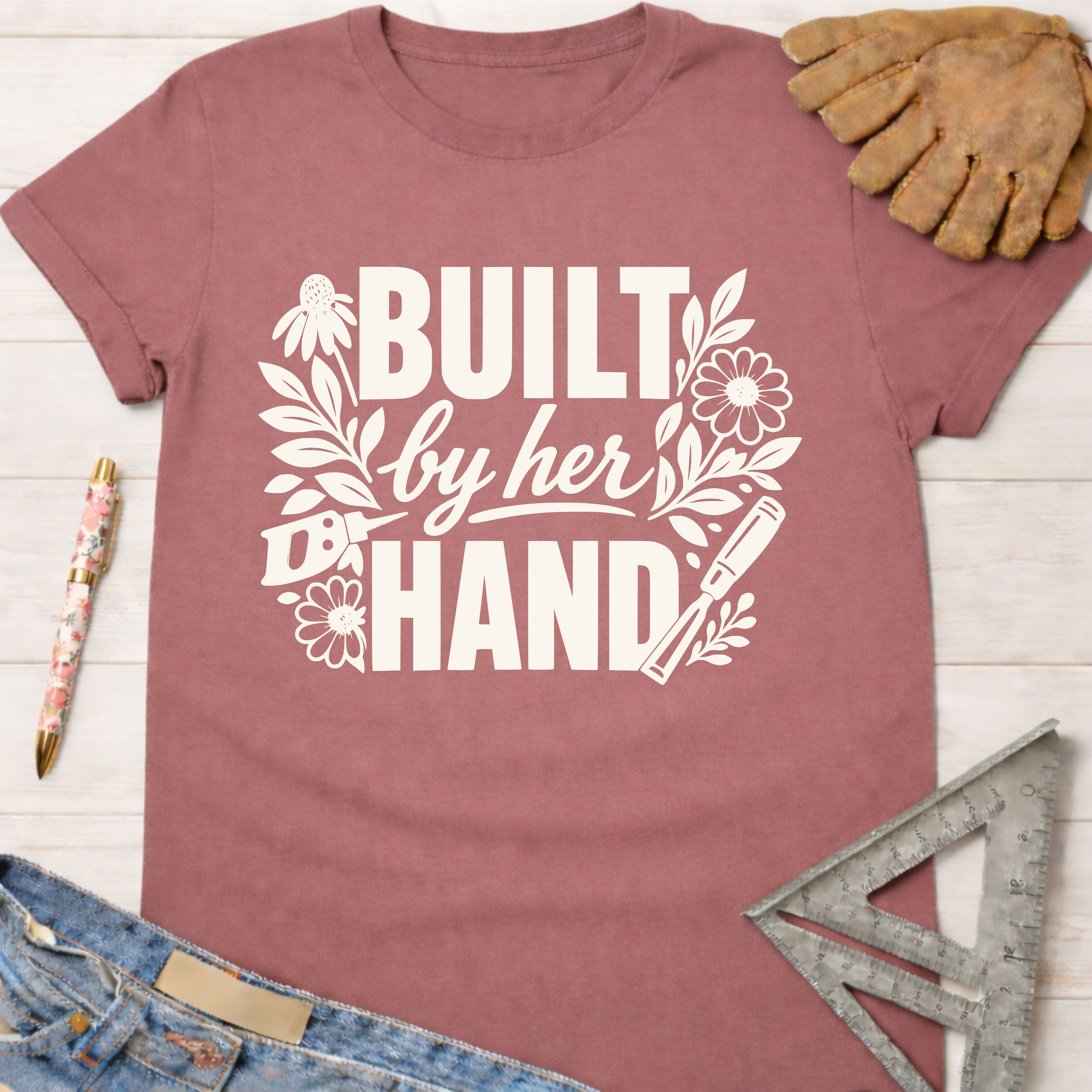Women's funny woodworking graphic tee shirt for female woodworkers, makers, and DIY builders — Sawdust & Ponytails. Mauve cotton tee with "Built by Her Hand" in white floral and tool graphic.