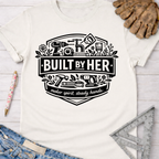 Women's funny woodworking graphic tee shirt for female woodworkers, makers, and DIY builders — Sawdust & Ponytails. Cream "Built By Her" graphic tee with tools.